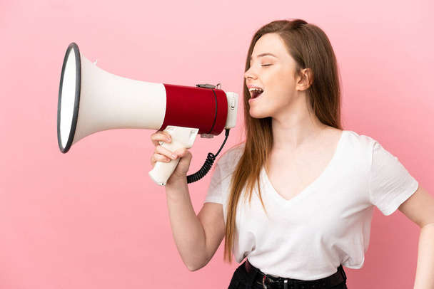Adolescente chica sobre aislado rosa fondo gritando a través de un megáfono para anunciar algo en posición lateral - Foto, Imagen