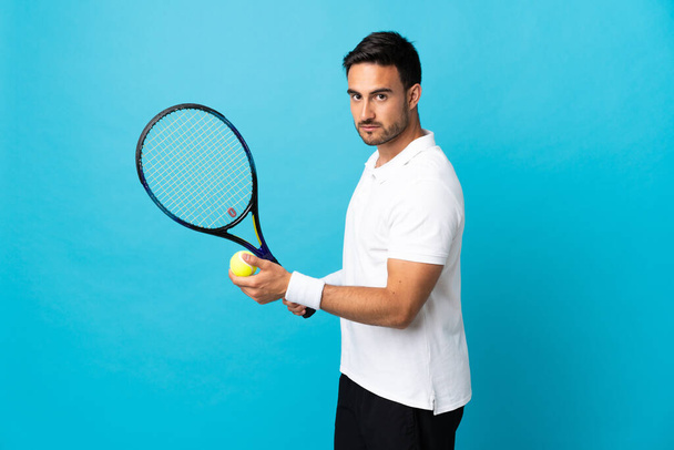 Jovem bonito homem isolado no fundo azul jogar tênis - Foto, Imagem