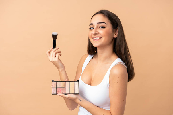 Young caucasian woman isolated on beige background with makeup palette and happy - Foto, imagen