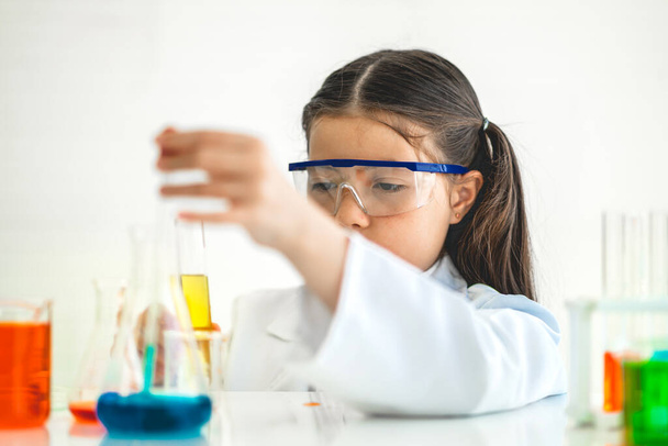 Cute little girl student child learning research and doing a chemical experiment while making analyzing and mixing liquid in glass at science class in school.Education and science concept - Photo, image