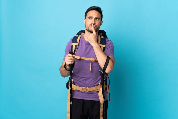 Young caucasian man with backpack and trekking poles isolated on blue background having doubts while looking up - Photo, Image