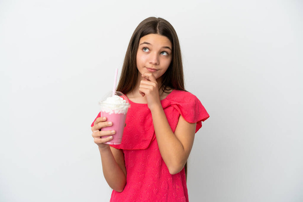 Маленька дівчинка з полуничним молочним коктейлем над ізольованим білим тлом і дивиться вгору
 - Фото, зображення