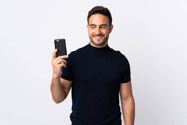 Young caucasian man using mobile phone isolated on white background with happy expression - Foto, afbeelding
