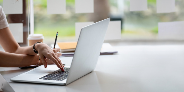 Przycięte zdjęcie ręka kobiety pisanie listy robi notatki w notatniku pracy lub uczenia się online z laptopem w domu - Zdjęcie, obraz
