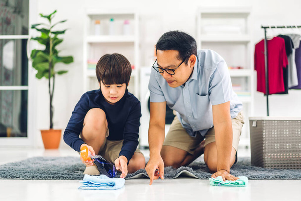 Ojciec uczy azjatyckie dziecko mały chłopiec syn używać środka dezynfekującego spray butelki czyszczenie i mycie podłogi wycieranie kurz szmatami podczas sprzątania domu razem w domu - Zdjęcie, obraz