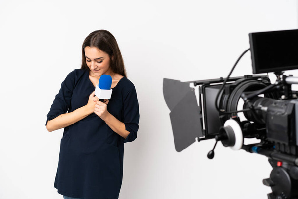 Reportera mujer sosteniendo un micrófono y reportando noticias aisladas sobre fondo blanco con un dolor en el corazón - Foto, imagen