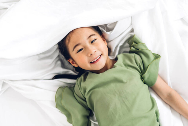 幸せな笑顔小さな子供アジアの女の子持っています楽しいです横に白いベッドと見てカメラに家 - 写真・画像