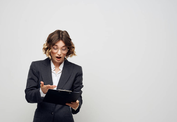 A woman with documents in a folder on a light background gestures with her hands - Фото, изображение