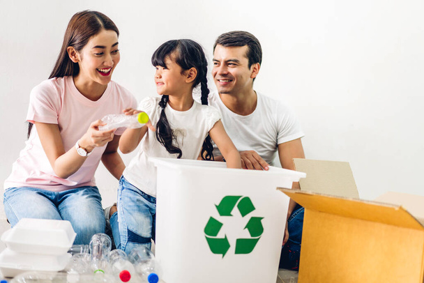 Happy smiling asian family father and mother with little asian girl having fun putting empty recycle plastic bottle garbage and reduce ecology environment into the recycle box - Photo, Image