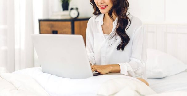 Młoda azjatycka kobieta relaksująca się przy użyciu laptopa w mroźny zimowy dzień w sypialni.kobieta sprawdzanie aplikacji społecznych i pracy.Komunikacja i koncepcja technologii - Zdjęcie, obraz