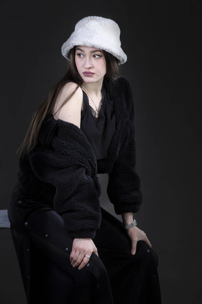 Beautiful stylish girl in a fur hat on a dark background. - Photo, image