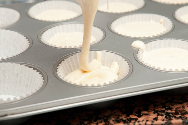 A white cream pouring into white cupcake molds - 写真・画像