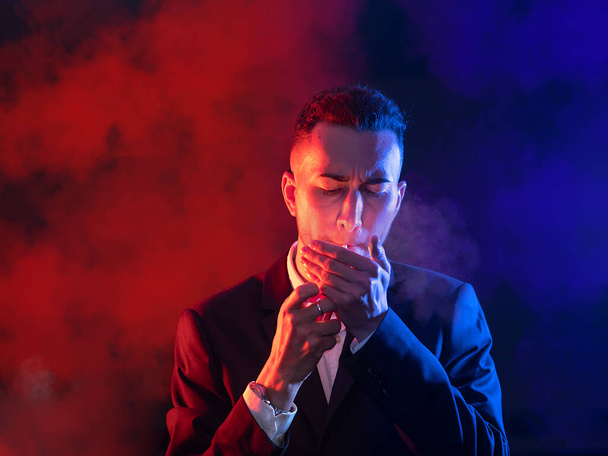 Eleganter junger Mann zündet sich eine Zigarre auf schwarzem Hintergrund an. Selektiver Fokus - Foto, Bild