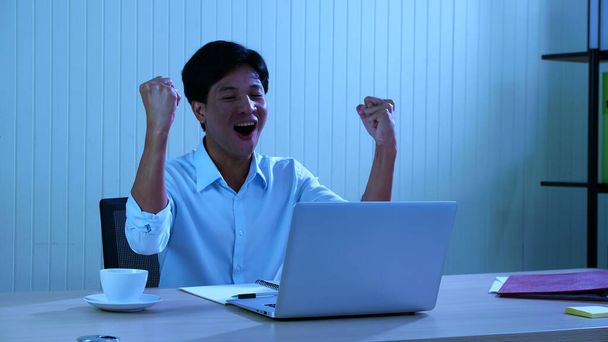 Γραφείο άνθρωπος κοίταξε το φορητό υπολογιστή και χαμογέλασε και σήκωσε το χέρι του, δείχνοντας σημάδια χαράς και ευτυχίας, Ενθουσιασμένος νεαρός άνδρας, κάνοντας χειρονομία ναι - Φωτογραφία, εικόνα
