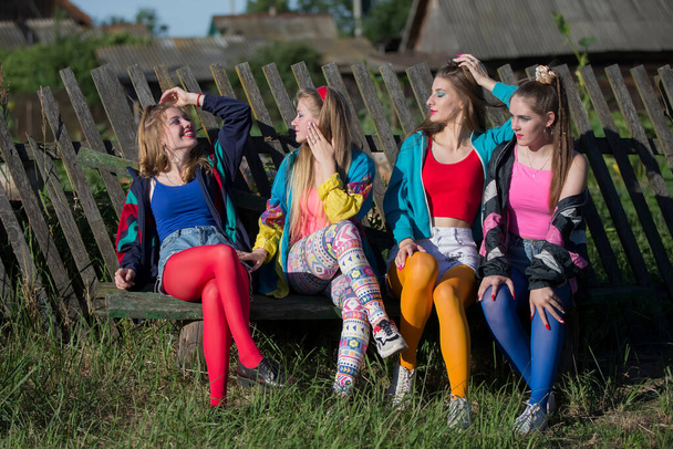 Jolies filles habillées dans le style des années 90 s'asseoir sur un banc par une clôture asymétrique. - Photo, image
