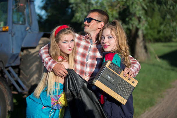 Funny man with cassette recorder hugs girls. People in the style of the nineties. - Photo, Image