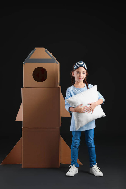 Roztomilé holčička s polštářem a lepenkové rakety na tmavém pozadí - Fotografie, Obrázek