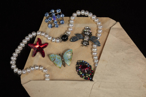 Κοσμήματα, καρφίτσες, χάντρες ξεχύθηκαν από ένα παλιό φάκελο αλληλογραφίας.. - Φωτογραφία, εικόνα