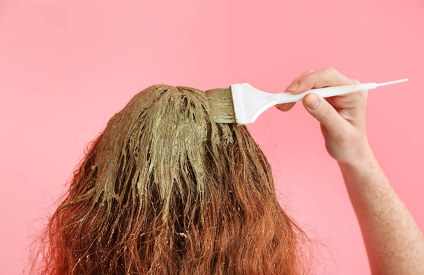 Young woman using henna hair dye on color background - Photo, Image