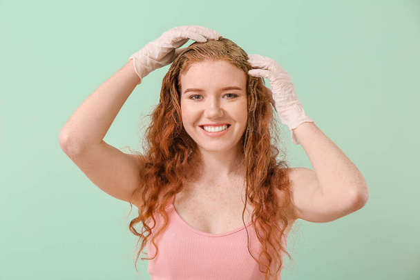 Mujer joven usando tinte de pelo de henna sobre fondo de color - Foto, Imagen