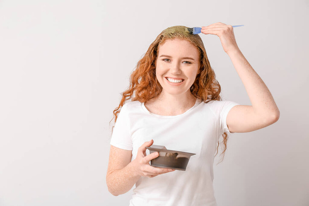 Junge Frau verwendet Henna-Haarfärbemittel auf hellem Hintergrund - Foto, Bild