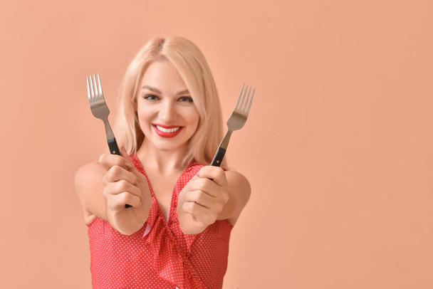 Mooie jonge vrouw met vorken op kleur achtergrond - Foto, afbeelding