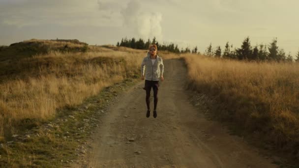 Männlicher Läufer wärmt die Beine vor dem Training. Mann springt in Bergen auf schmutzige Straße - Filmmaterial, Video