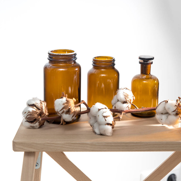 Three pharmacy bottles and a branch with cotton flowers on a wooden stool surface on a white background. Copy space - Fotó, kép