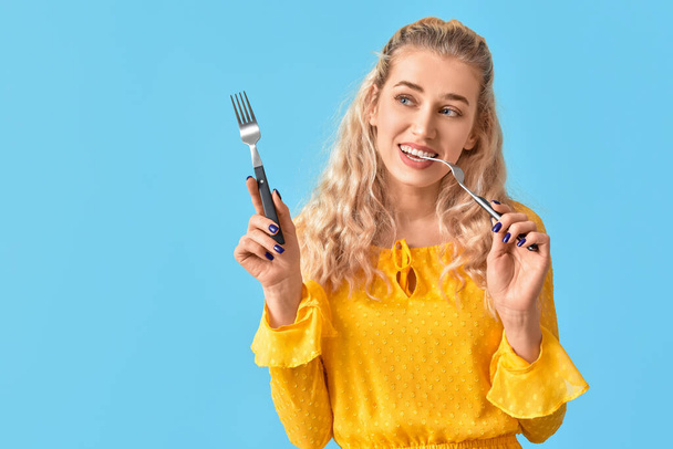 Beautiful young woman with forks on color background - 写真・画像