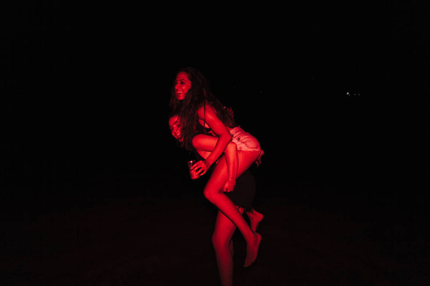 Grupo de mujeres jóvenes divirtiéndose en una fiesta junto al lago por la noche con una luz roja - Foto, imagen
