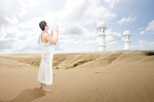 Asian Muslim man in ihram clothes standing and praying while raised arms on the desert - Foto, immagini