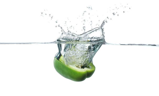 Falling of fresh cut bell pepper into water against white background - Foto, Imagen