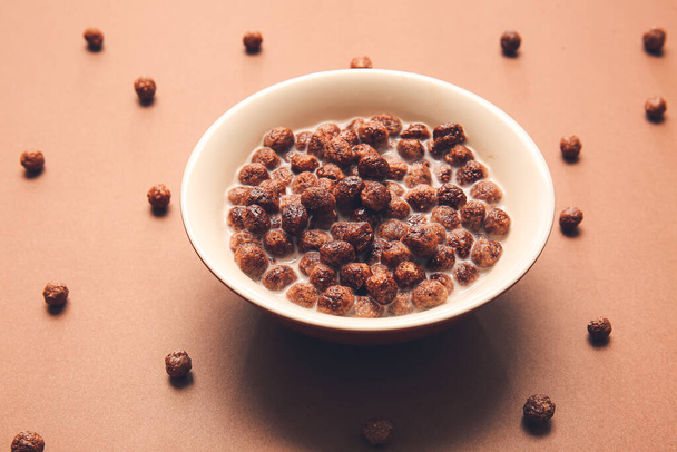 Bowl with chocolate corn balls and milk on color background - Fotó, kép