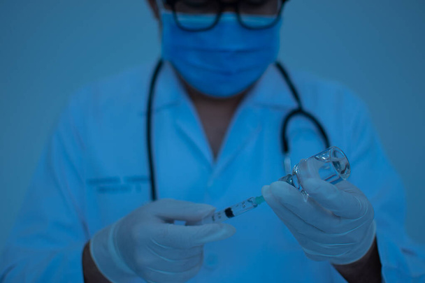 Los médicos están experimentando con la vacunación contra el coronavirus. Los científicos están usando una jeringa. Un hombre con una máscara sostiene una jeringa y un frasco de vacuna. Concepto del ensayo con vacuna de laboratorio. - Foto, imagen