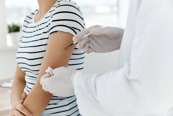 mannelijke arts in een witte vacht die een patiënt injecteert in de schouder covid vaccinatie - Foto, afbeelding