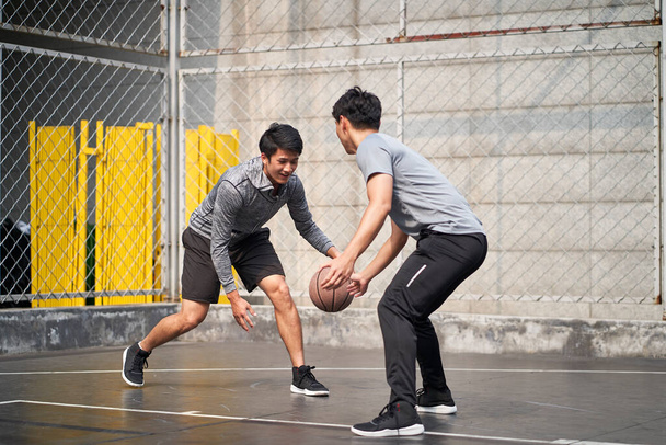 twee jonge aziatische volwassen mannen spelen een-op-een basketbal op het buitenveld - Foto, afbeelding