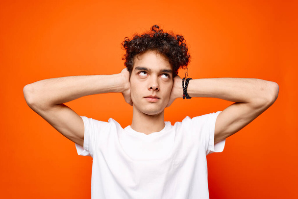 guy in a white t-shirt with curly hair holding his head emotions orange background - Photo, Image