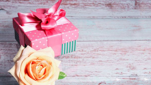 Ένα κουτί δώρου με ροζ φιόγκο σε ξύλινο φόντο, αντίγραφο του χώρου κειμένου ένα τριαντάφυλλο γύρω από το ξενοδοχείο. - Φωτογραφία, εικόνα