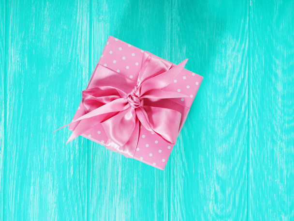 Een geschenkdoos met een roze strikje op een houten achtergrond, kopie van de tekstruimte. - Foto, afbeelding