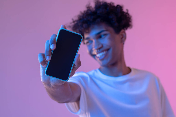 Headshot of curly-haired smiling guy with a smartphone - Fotoğraf, Görsel