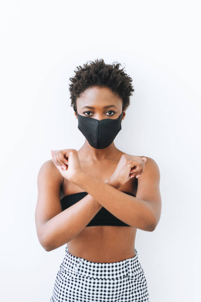 Bella giovane donna afroamericana in top nero e maschera isolata sullo sfondo bianco, stop concetto coronavirus - Foto, immagini