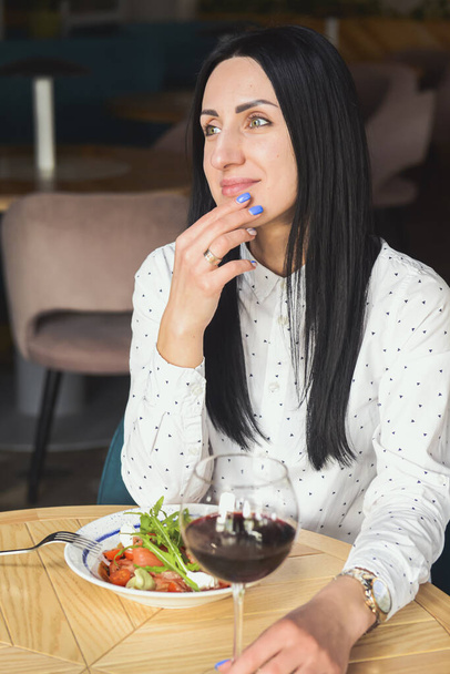 Young attractive woman having a healthy lunch in restaurant. Caucasian female with black hair dining. Eating out concept, eating alone in restaurant due to Covid-19 pandemic. - Photo, image