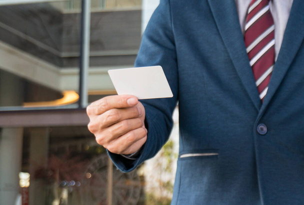 Επιχειρηματίας δείχνει κενό επαγγελματική κάρτα και κρατώντας έξυπνο τηλέφωνο.Επιχειρηματίας κρατώντας λευκό κενό χώρο κάρτα για κείμενο. οθόνη του προϊόντος - Φωτογραφία, εικόνα