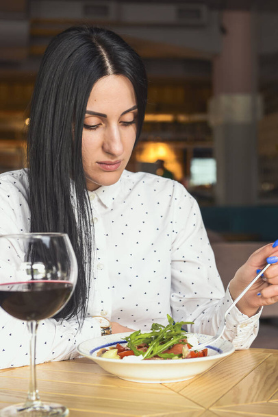 Young attractive woman having a healthy lunch in restaurant. Caucasian female with black hair dining. Eating out concept, eating alone in restaurant due to Covid-19 pandemic. - Foto, Imagem