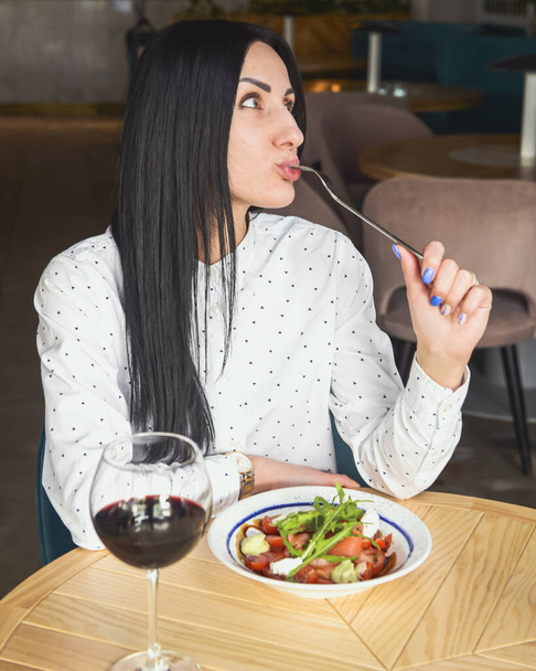 Young attractive woman having a healthy lunch in restaurant. Caucasian female with black hair dining. Eating out concept, eating alone in restaurant due to Covid-19 pandemic. - Fotó, kép