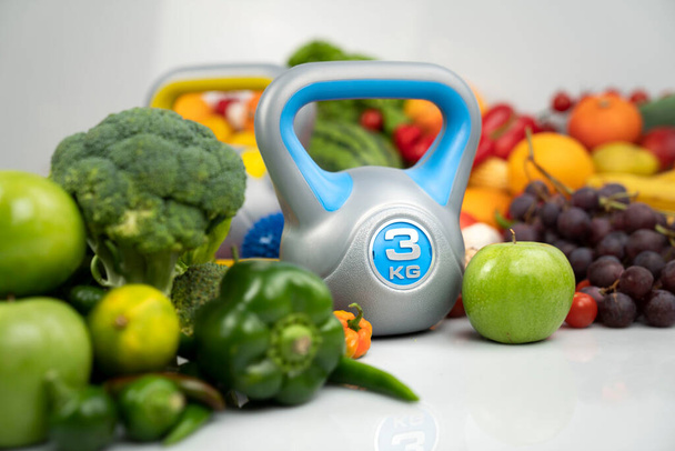 Fitness-Konzept. Gesunde Ernährung: Obst und Gemüse. Geräte für Fitnessübungen: Wiegegerät und Hanteln. Weißer Hintergrund. - Foto, Bild