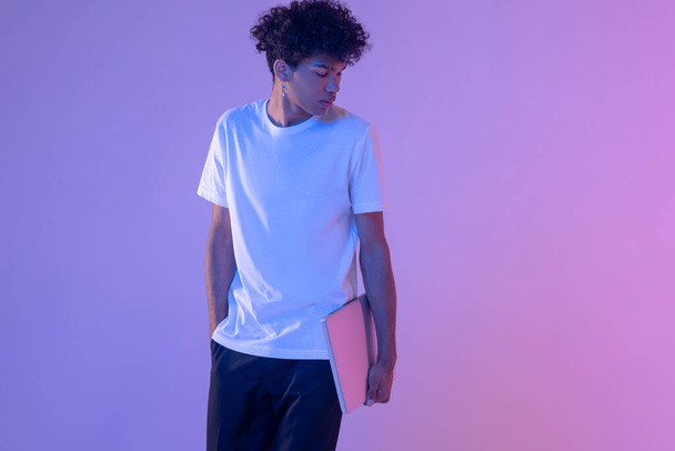 Curly-haired young guy in white tshirt with a laptop - 写真・画像