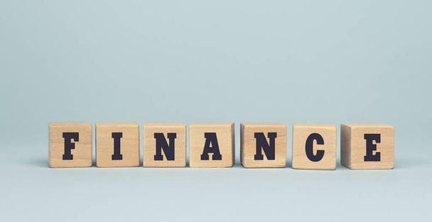 The word FINANCE made from wooden cubes on blue background. Conceptual photo - Photo, image