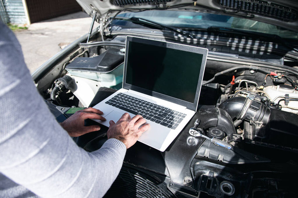 um homem faz um diagnóstico do carro com um laptop sob o capô - Foto, Imagem
