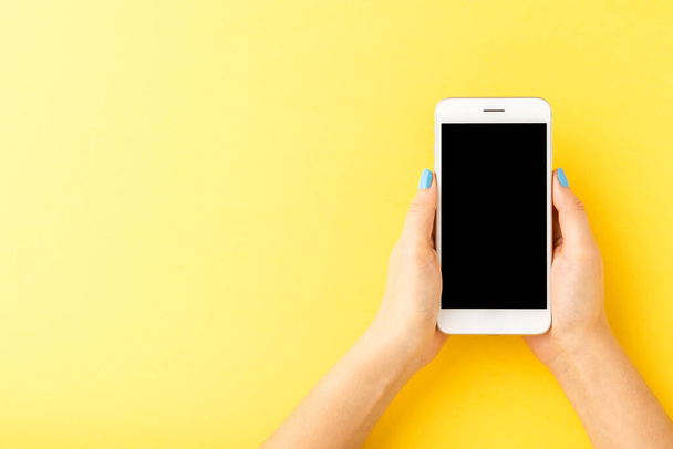 Female hands holding smart phone with empty screen on yellow background. Top view - Фото, зображення